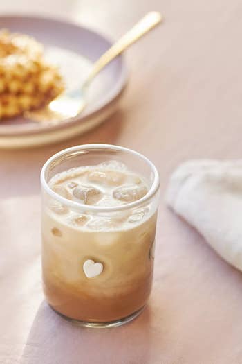Iced coffee in a glass with a heart design, placed on a table with a waffle and a napkin in the background