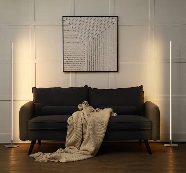 the two column lamps one on each side of a charcoal gray couch 