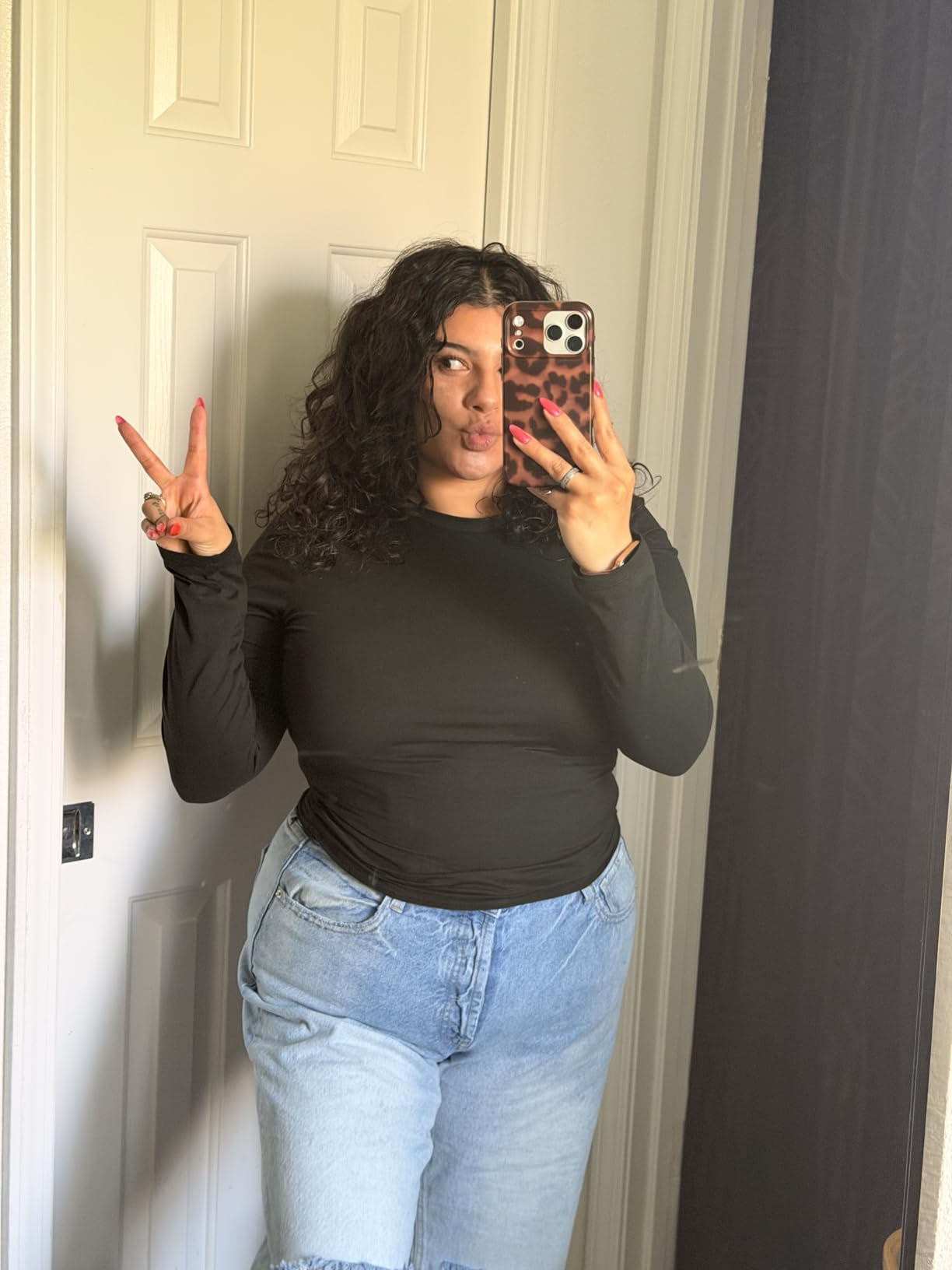Person taking a reflector  selfie, wearing a achromatic  long-sleeve apical  and bluish  jeans, making a bid    motion   with 1  hand