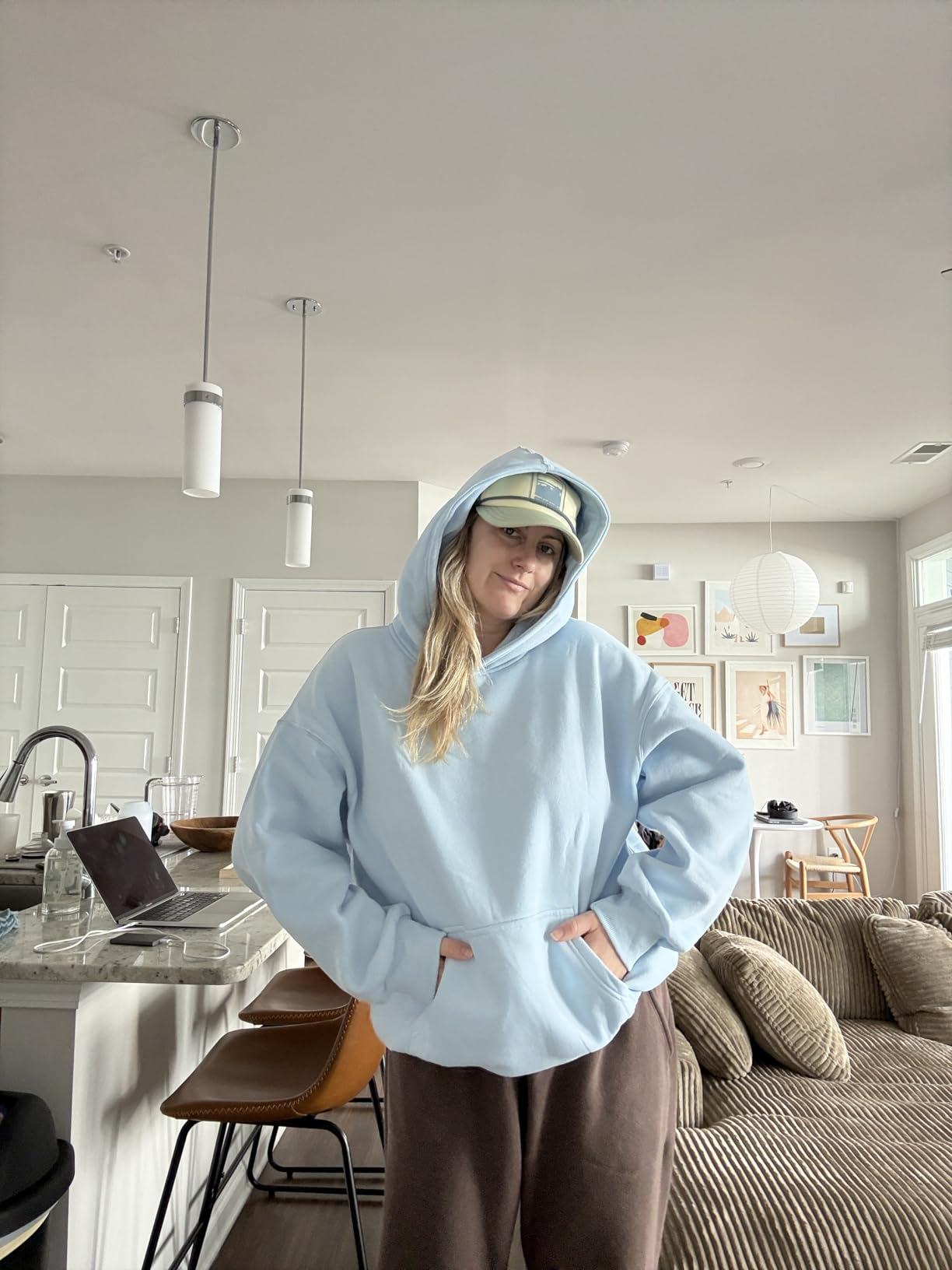 Person successful  a relaxed room  mounting  wearing a cozy hoodie, cap, and comfy  pants, adjacent  to a room  antagonistic  with stools and decor