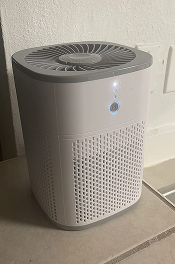 Reviewer image of white small air purifier on tile floor with fan on top