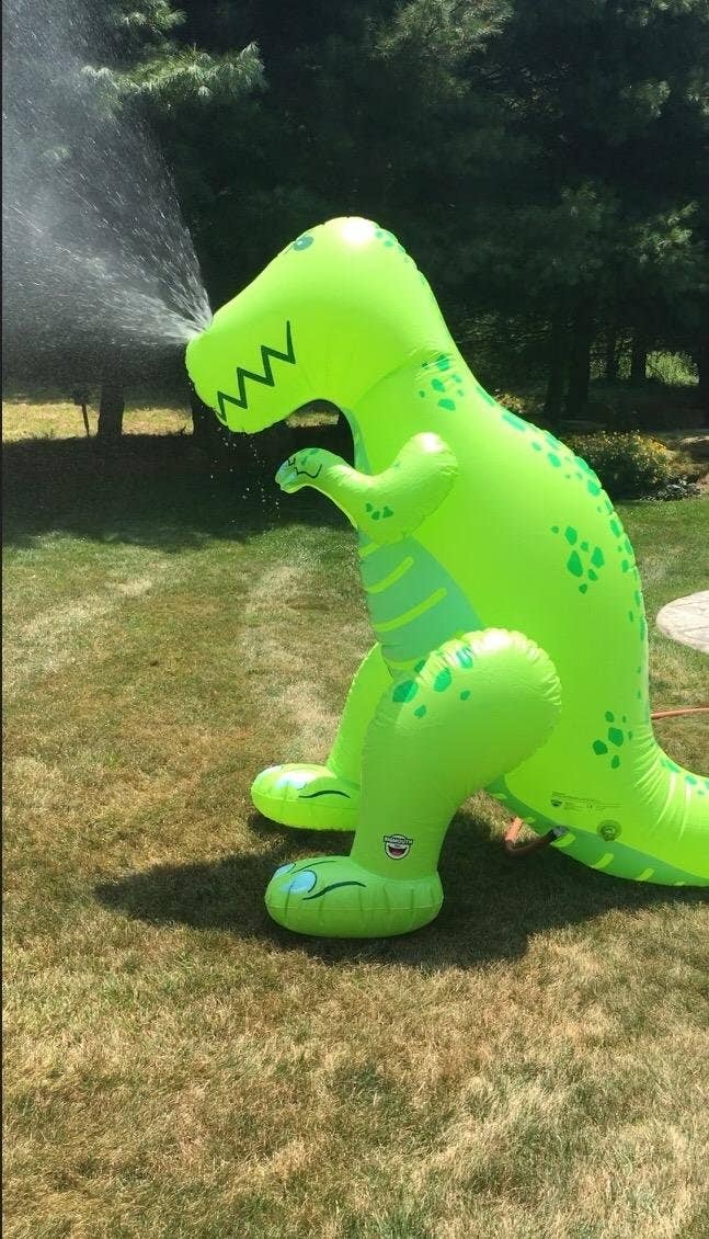 Inflatable dinosaur sprinkler toy in a garden for outdoor fun