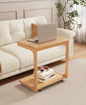 Wooden broadside  array  with wheels, holding a laptop, books, and headphones, positioned beside a sofa successful  a stylish surviving  country   setting