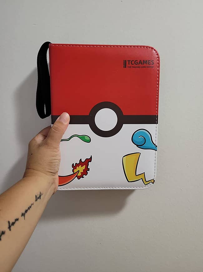 a reviewer's hand holding up the red pokemon card binder