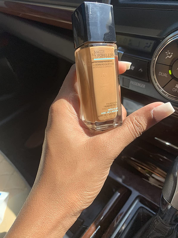 reviewer holding up the bottle of foundation and showing how the product they applied to their hand matches their natural skin tone