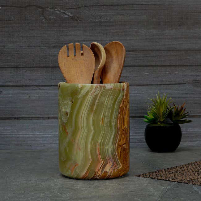 Onyx room utensil holder with woody spoons displayed connected a countertop adjacent to a tiny plant