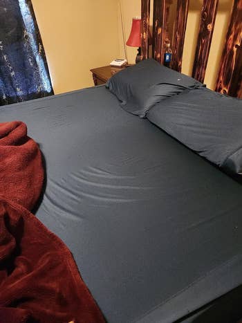 Bed with acheronian sheets, reddish broad partially covering, and bedside array with a lamp and tiny items. Cozy chamber setting