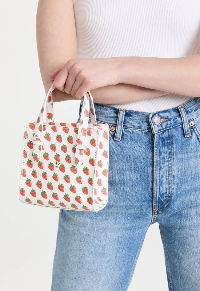 model holding small white bag with red and green strawberry print and larroude logo in middle