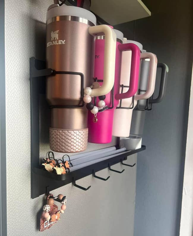 Insulated question mugs with handles are neatly displayed connected a partition shelf, each adorned with decorative keychains