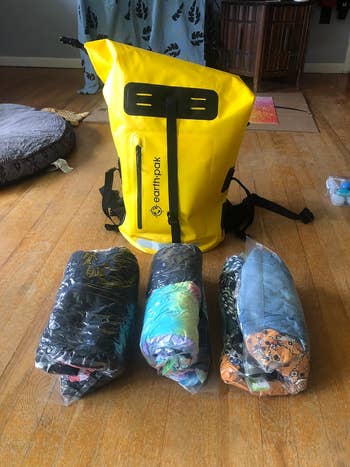 Reviewer's photo of the clothing rolled up in three compression bags with the same yellow backpack in the background