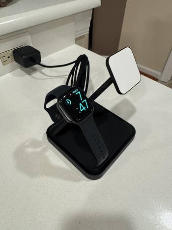 Smartwatch charging on a sleek stand with attached wireless pad, set on a countertop, highlighting modern tech organization for shopping enthusiasts