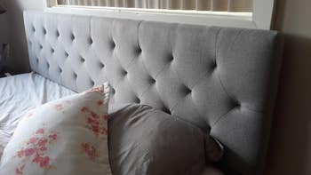 Reviewer image of gray tufted headboard against a white sheeted bed 