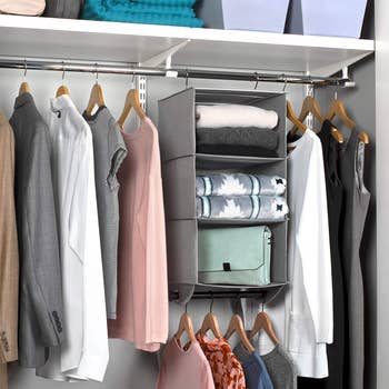 the hanging organizer with three shelves in a closet and clothes hanging below