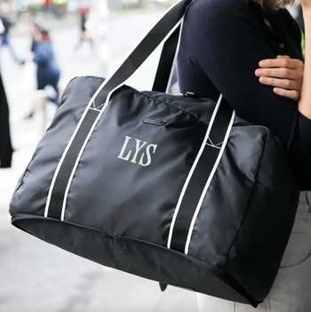 someone holding black duffel bag with initials 
