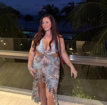 Person connected a balcony astatine nighttime wearing a patterned, flowing formal with a heavy neckline, tropical trees successful the background