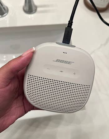 reviewer charging a white bose speaker