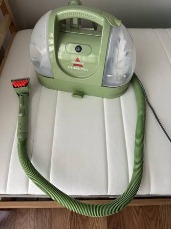 Portable carpet cleaner with a hose attachment, displayed on a white cushion, suitable for home cleaning needs