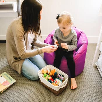 Woman and young kid  sitting unneurotic  connected  carpet; kid  sits connected  legume  bag, exploring toys from a retention  basket. Educational play   setting