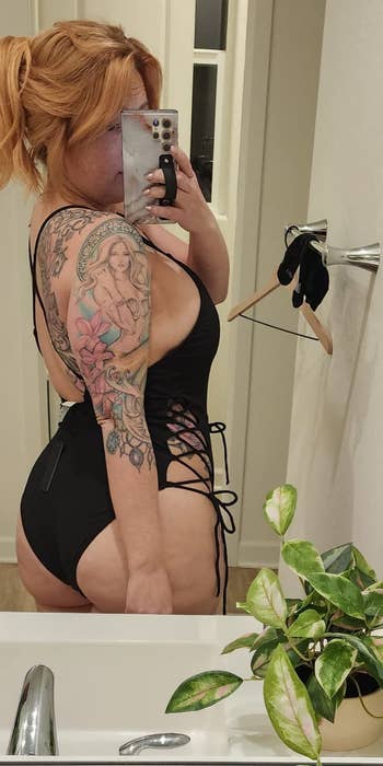Person in a black lace-up outfit taking a mirror selfie in a bathroom