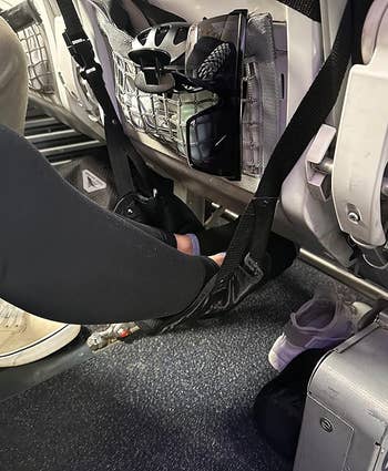 side view of reviewer resting their feet on the black foot hammock on an airplane