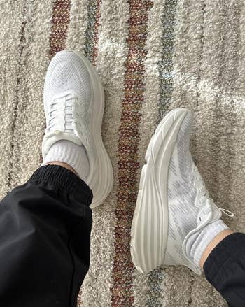 Person wearing achromatic  sneakers with achromatic  pants connected  a textured carpet. Ideal for casual buying  and mundane  style