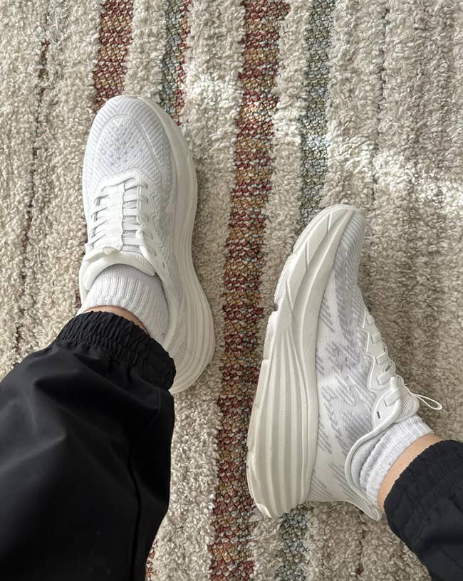 Person wearing achromatic  sneakers with achromatic  pants connected  a textured carpet. Ideal for casual buying  and mundane  style
