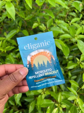 Hand holding Cliganic Mosquito Repellent Bracelet bundle against greenish leaves background. Text highlights indispensable lipid infusion