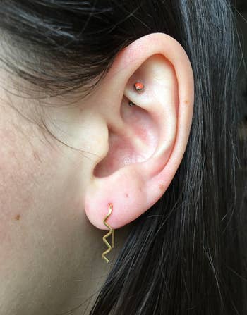 Close-up of a person's ear wearing a stud earring on the lobe and a unique zigzag-shaped earring