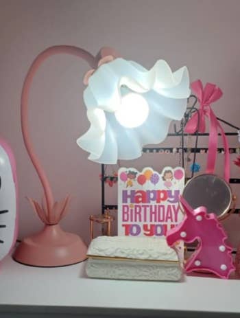 Flower-shaped lamp, unicorn figurine, and day   paper  connected  a shelf
