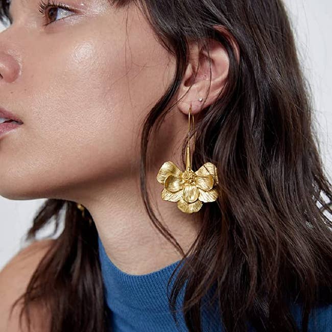 model wearing long gold earrings with flower petal design at bottom