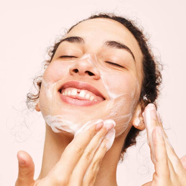 A person smiling with foaming cleanser applied to their face