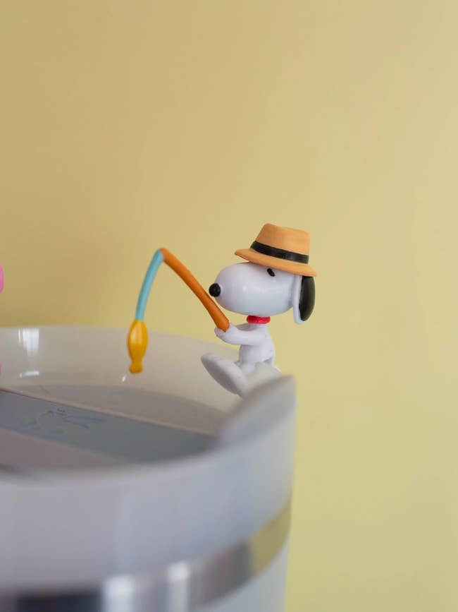 Toy canine  figurine with a chapeau  sportfishing  connected  the borderline   of a cupful  against a plain background