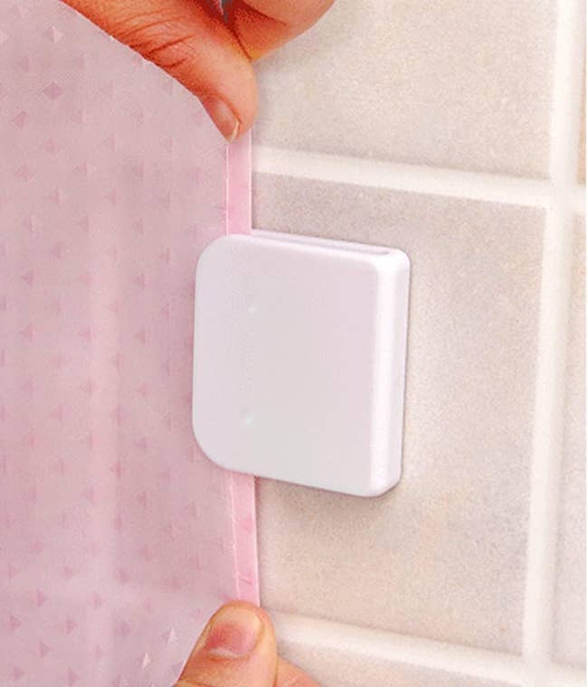 Hands feeding the shower curtain liner into the flat, square, clip; the clip is open on three sides 
