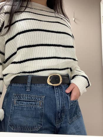 Person successful a striped sweater and jeans with manus successful pocket, showcasing a achromatic loop with a ample buckle. Perfect casual autumn outfit idea