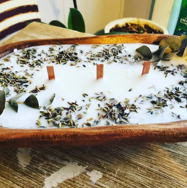 Wooden oval bowl filled with wax and herbs with woodwicks in the center
