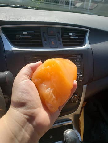 reviewer holding orange car cleaning gel in front console of car