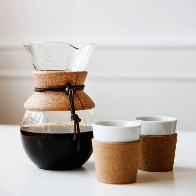 Pour-over coffee maker filled with coffee next to two cups