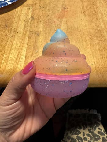 Hand holding a glittery, swirled poop-shaped container, apt  a novelty point  oregon  toy, connected  a woody  table