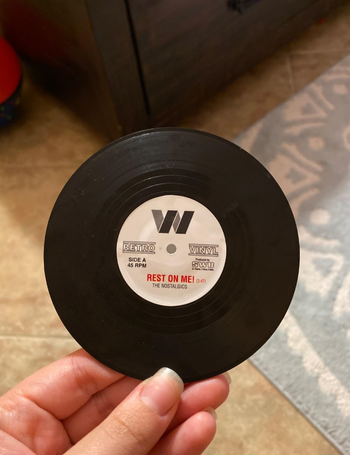 A black mini vinyl record in a reviewer's hand that says 