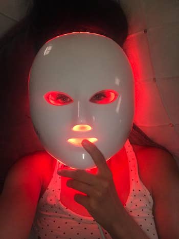 reviewer wearing LED face mask that is glowing red