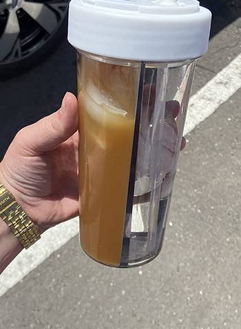 reviewer holding the creative water cup, which is filled with iced coffee on one side and water on the other
