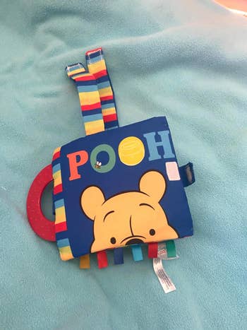 Child's plush book with Winnie the Pooh's face and colorful tags for sensory play