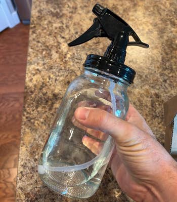 A manus holding a transparent spray vessel with a achromatic nozzle, connected a room countertop