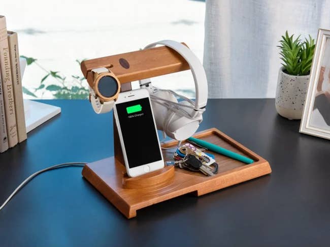 the wood valet tray and charging station with an iPhone charging, a watch and headphones hanging, and a ring of keys sitting in the tray