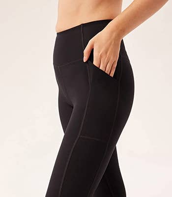 a model putting their hand in the side pocket of the black leggings