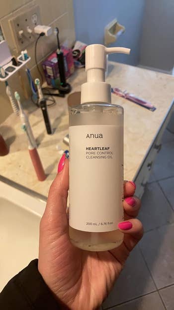 Person holding a bottle of Anua Heartleaf 77% Soothing Cleanser in a bathroom setting