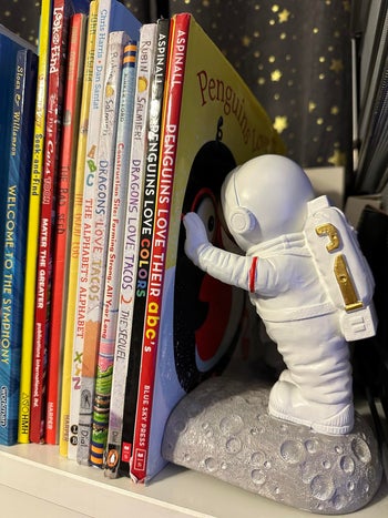 Astronaut figure bookend supporting a row of children's books on a shelf