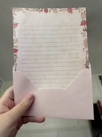 Person holding floral stationery with lined insubstantial  partially pulled from a pinkish  envelope