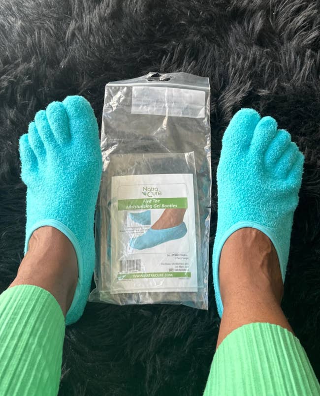 Person wearing turquoise moisturizing gel socks with product packaging on a furry surface