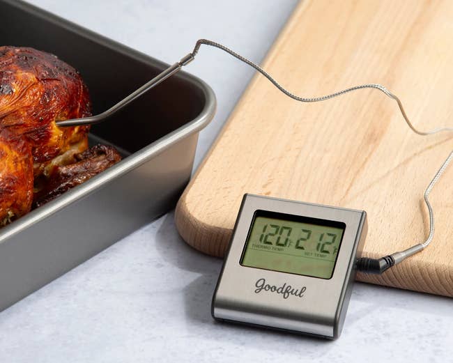 The thermometer with its probe inserted into cooked chicken and the display leaning against a cutting board while showing the temperature on the screen